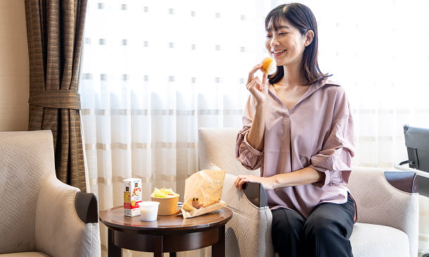 お部屋でゆったりしながら、リラックスな環境で朝食を食べる女性。